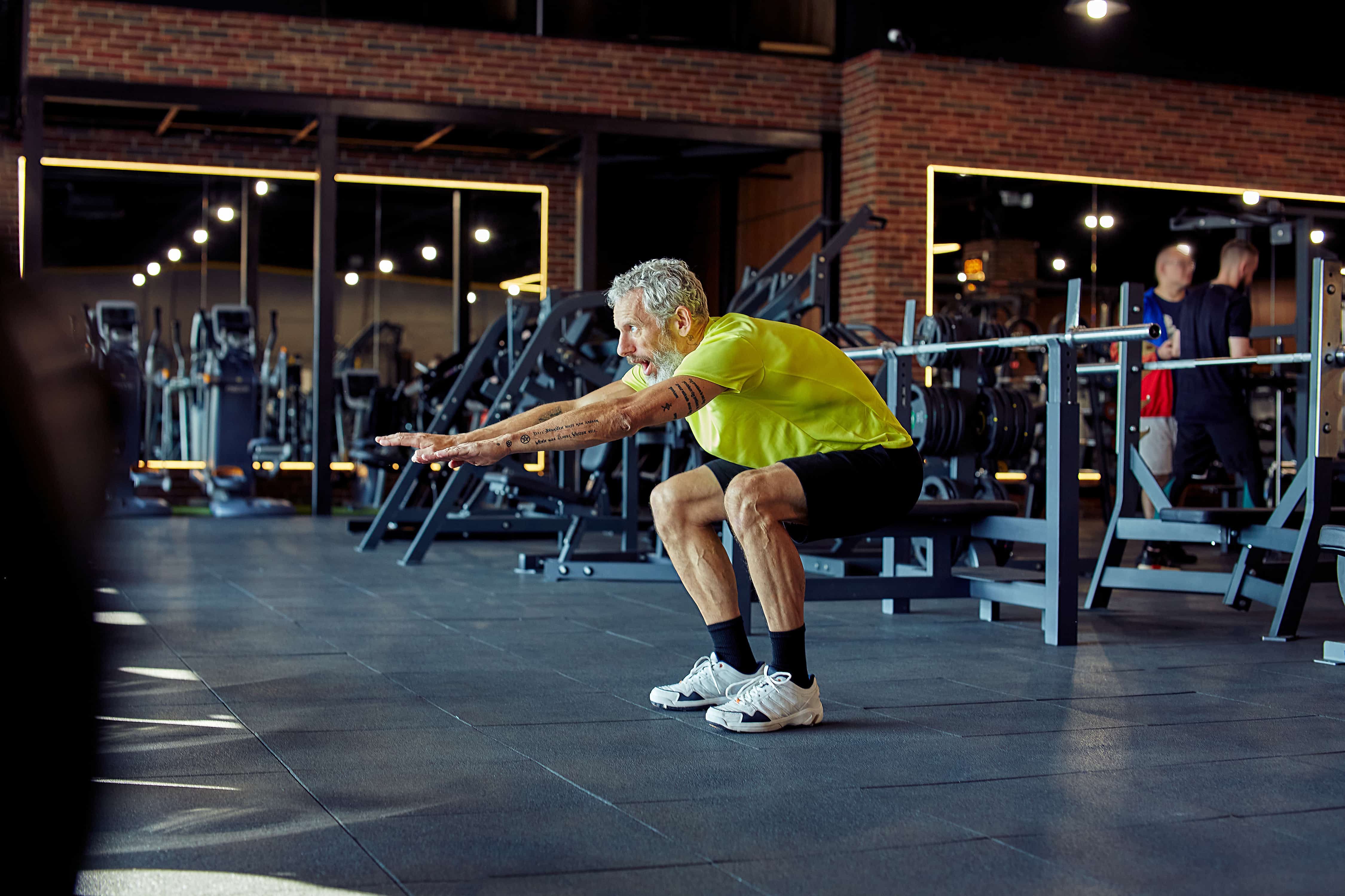 Post theme photo. Elderly man performing squat in a gym.